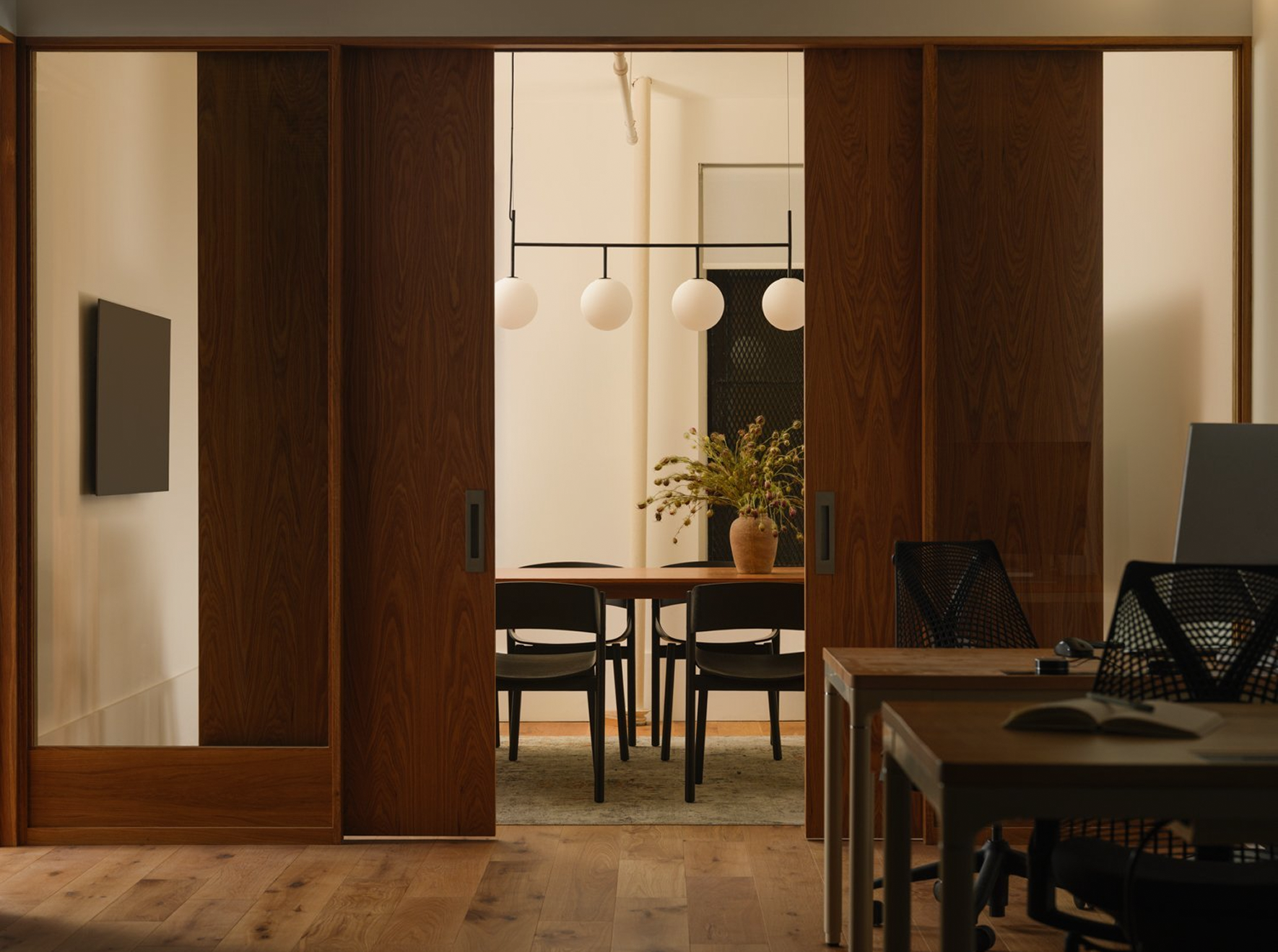 View through open walnut sliding doors into a dining room with globe pendant lights