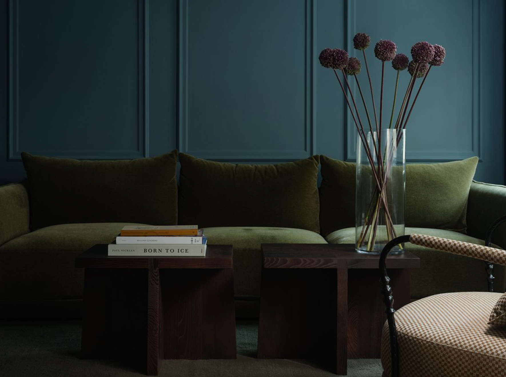 Sitting room with an olive-green velvet sofa against deep blue-green panelled walls and a vase of allium flowers