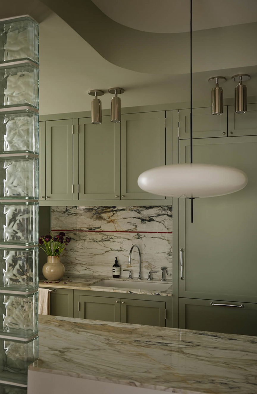 Sage-green kitchen with a veined-marble backsplash and island beside a glass-block wall