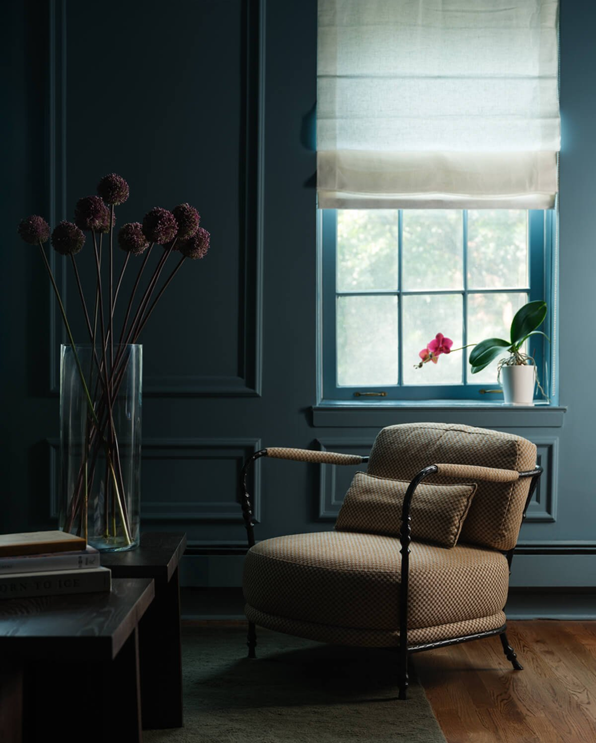 Deep blue-green panelled sitting room with a checkered-upholstered armchair beside the window