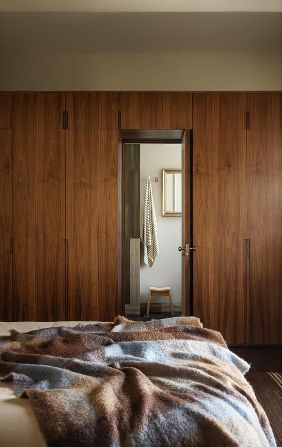 Bedroom with a full wall of walnut wardrobes and an open door to an ensuite bathroom