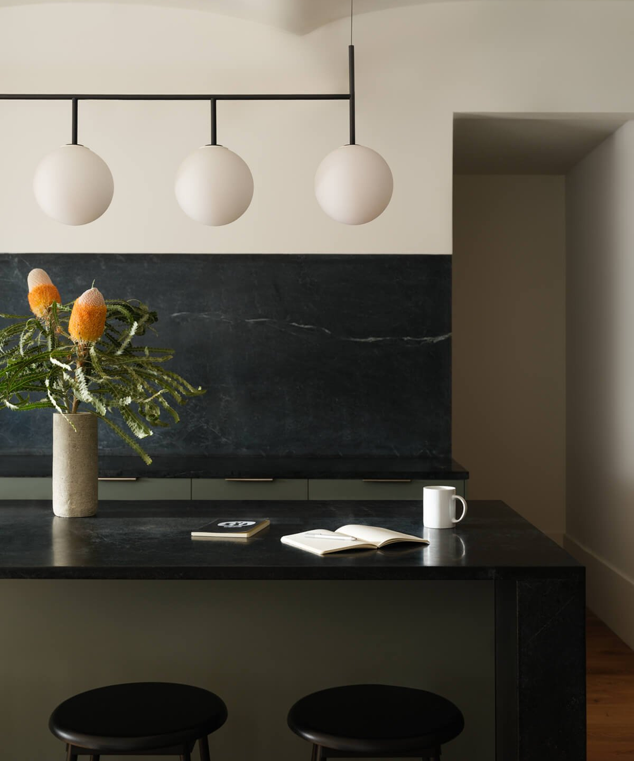 Kitchen with a black soapstone waterfall island and backsplash beneath a row of globe pendant lights