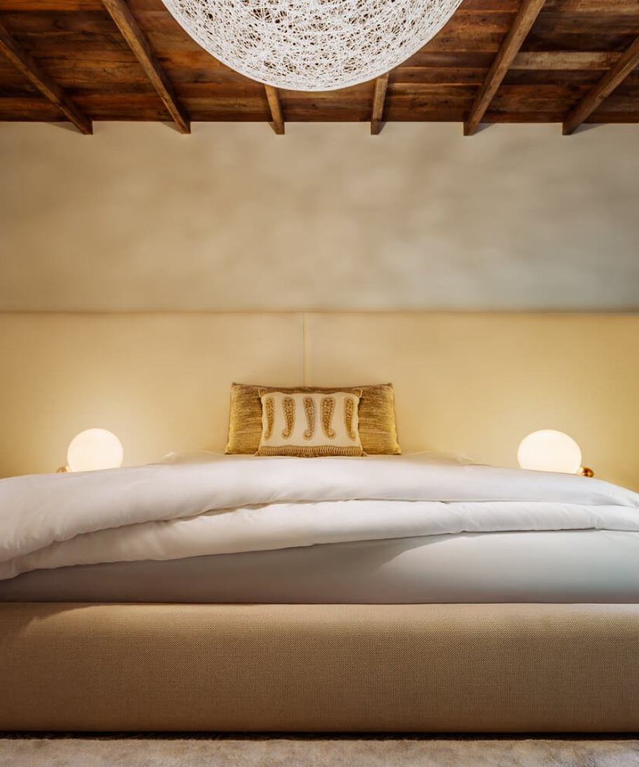 Bedroom with an upholstered cream bed and a woven pendant light beneath an exposed wood-beam ceiling