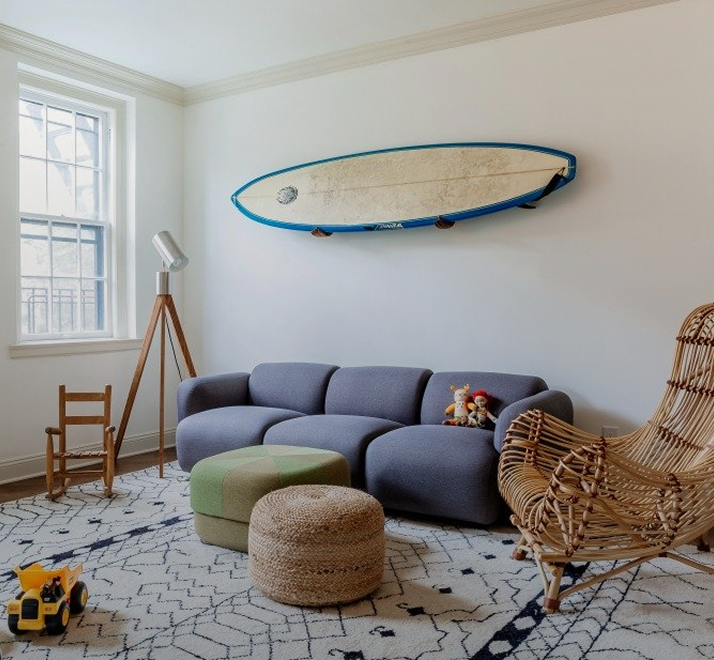 Playroom with a slate-blue sofa, a surfboard on the wall and a jute pouf