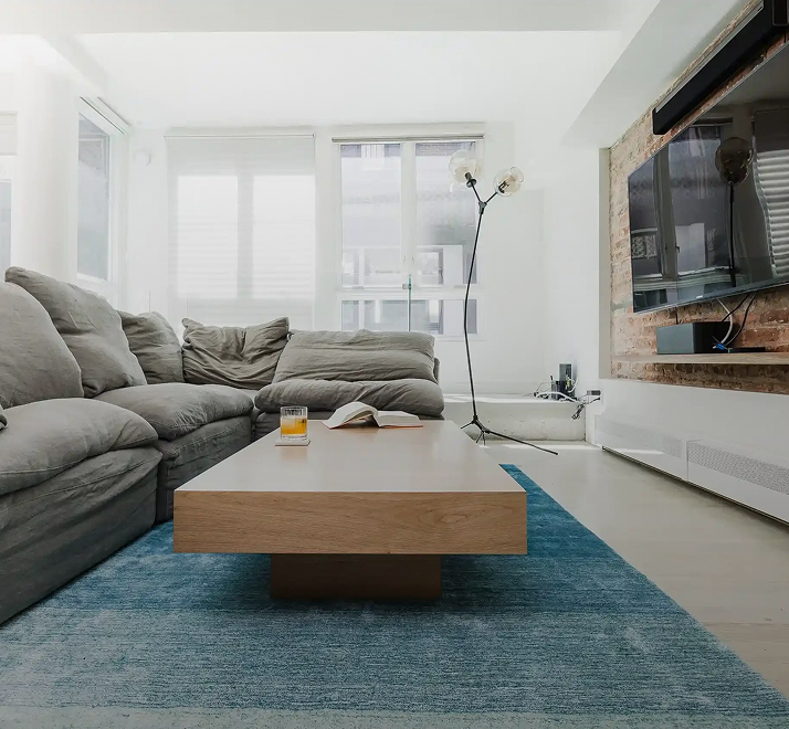 Living room with a grey sectional, a blue rug and an exposed-brick TV wall