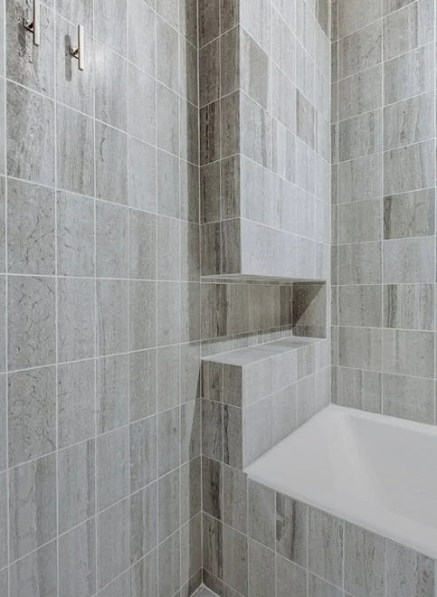 Grey stone-tiled shower niche beside a white bathtub